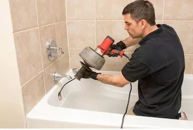homem accroupi dans une baignoire qui utilise un furet électrique pour déboucher la canalisation